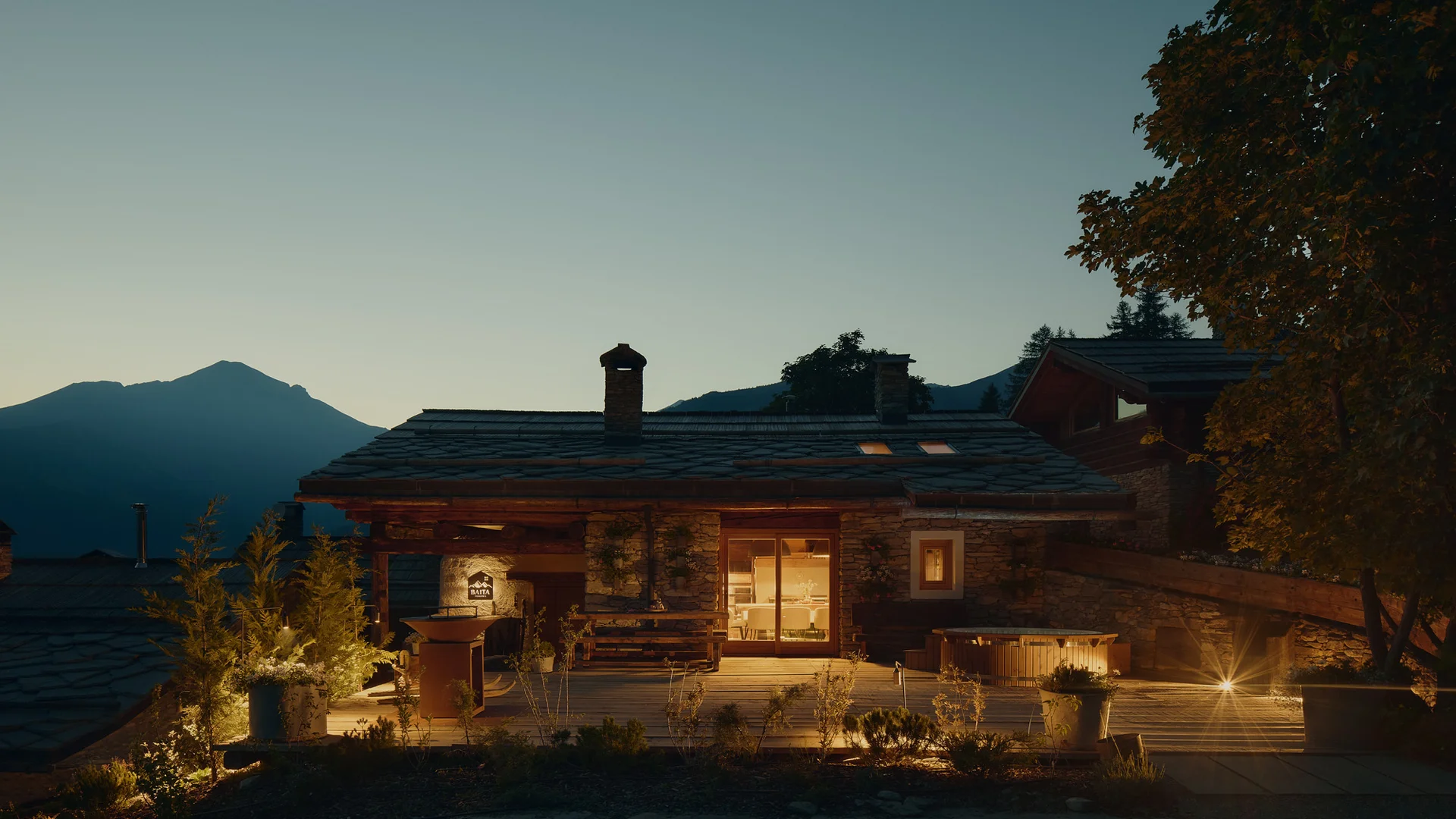 Chalet illuminato al crepuscolo, con terrazza e montagne sullo sfondo