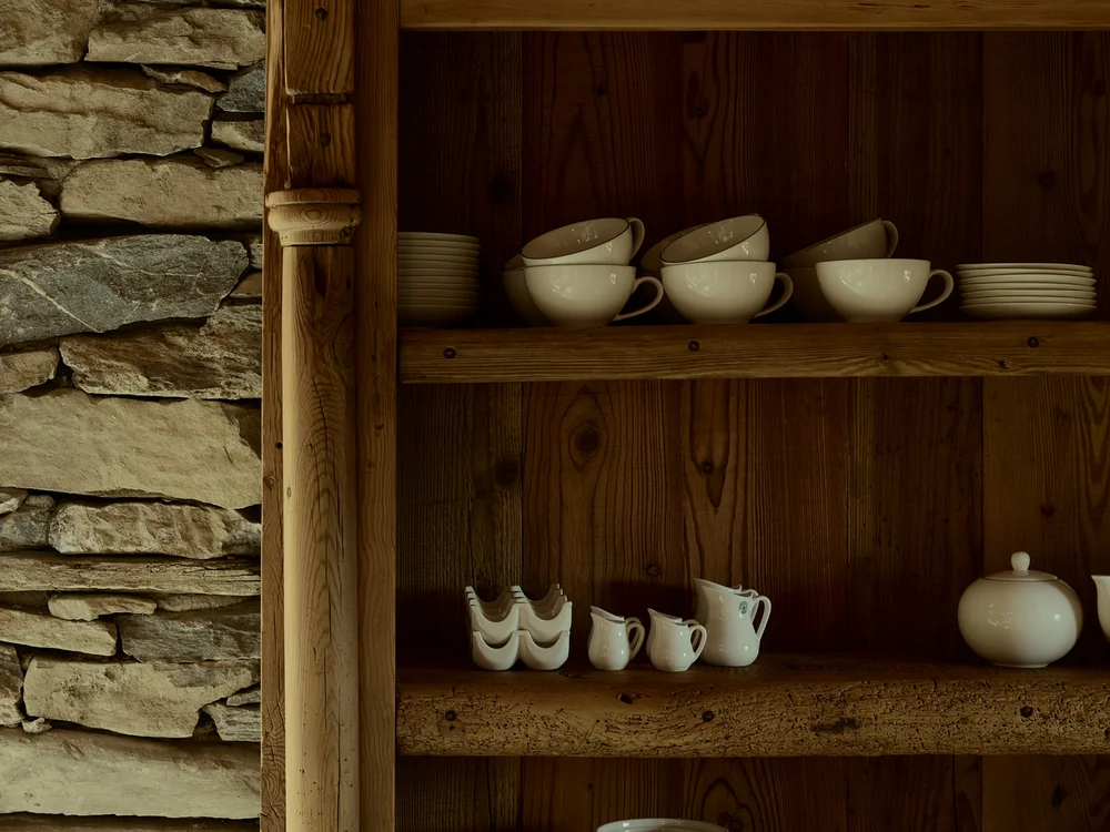 Baita Horres · Luxury Mountain Chalet · Bardonecchia Credenza rustica in legno con stoviglie in ceramica accanto a una parete di pietra