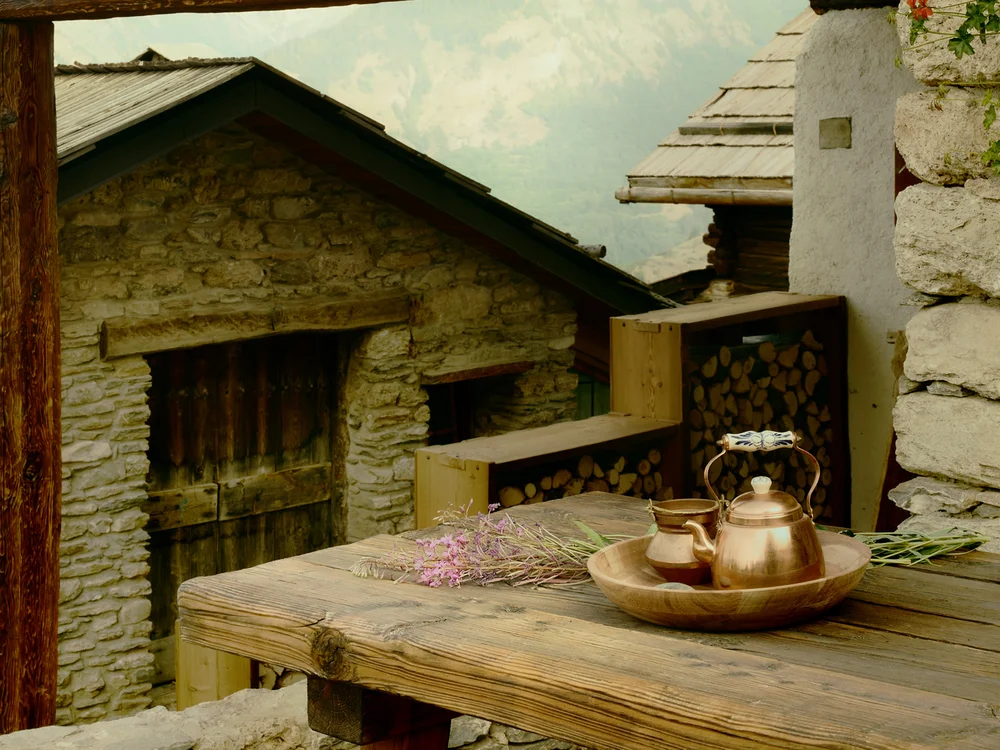 Baita Horres · Luxury Mountain Chalet · Bardonecchia Tavolo rustico in legno con teiera di rame e tazze in un cortile tra edifici in pietra