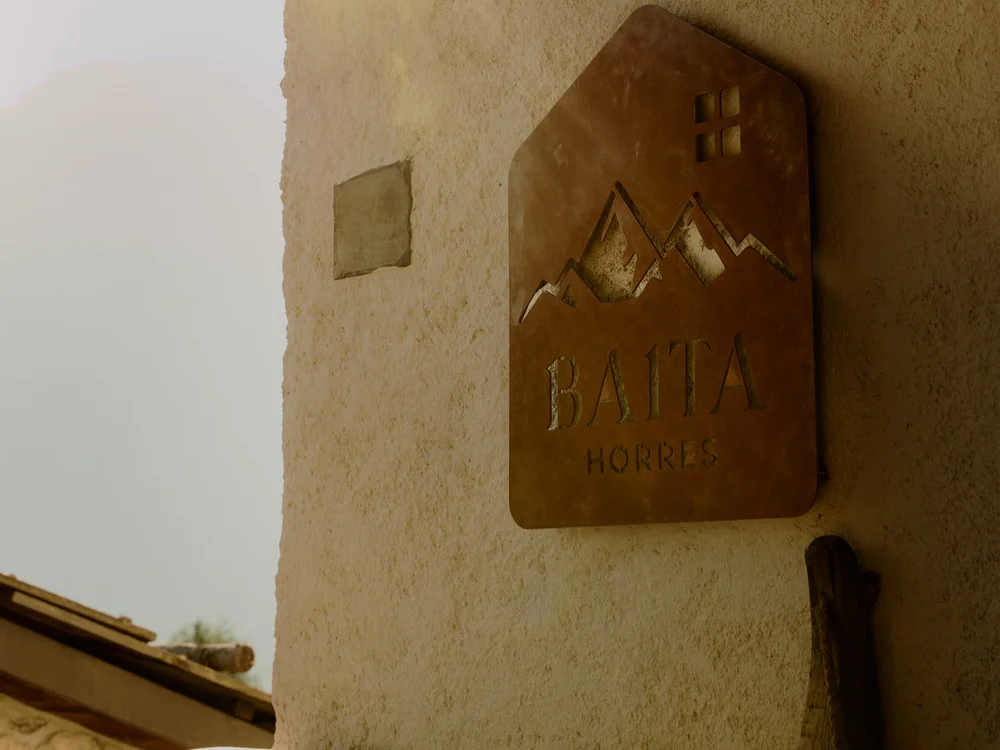 Baita Horres · Luxury Mountain Chalet · Bardonecchia Targa in legno con montagne e scritta Baita Horris su una parete rustica illuminata dal sole