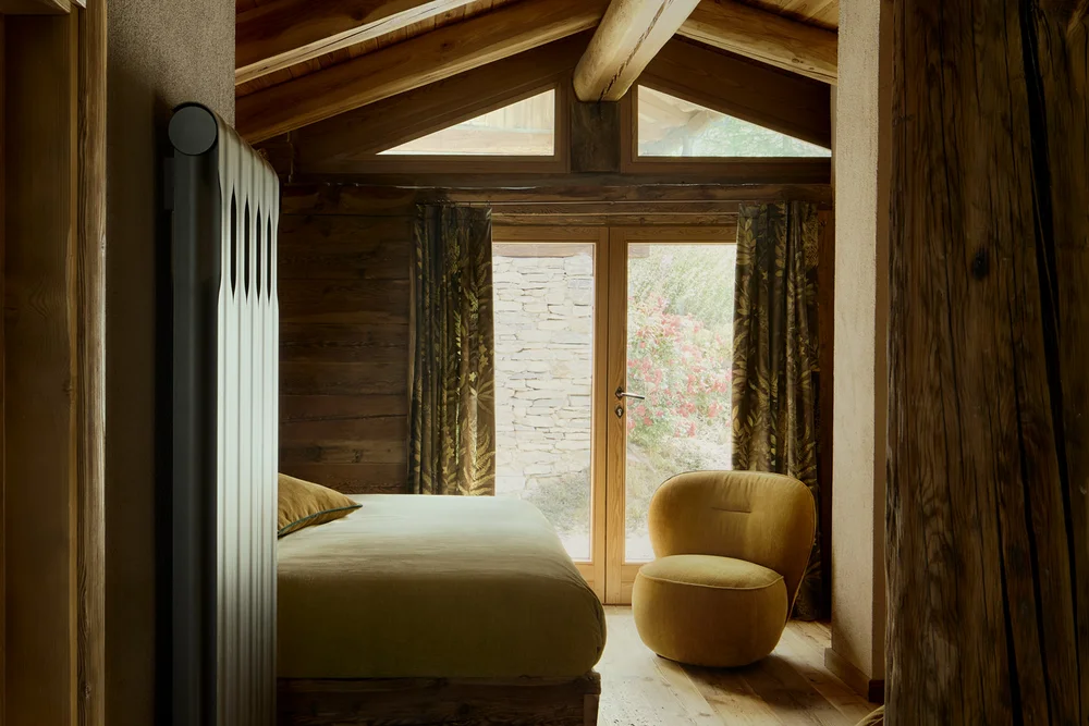 Camera da letto in legno con travi a vista, letto, poltrone e porta a vetri