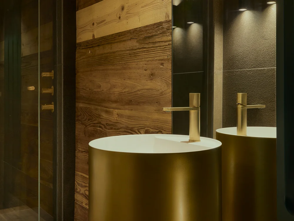 Baita Horres · Luxury Mountain Chalet · Bardonecchia Lavabo cilindrico color ottone con piano bianco in un bagno rivestito in legno
